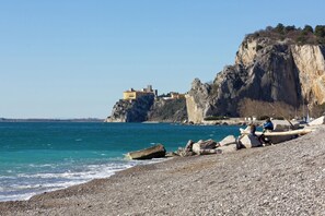 Ein felsiger Strand mit einer hohen Klippe und einem Gebäude darauf.