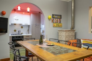 A dining area with a wooden table, chairs, a wine bottle, and a pizza.