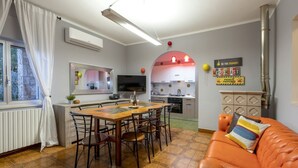 A dining area with a wooden table and chairs, a kitchen with a red arch, and a living area with an orange sofa.