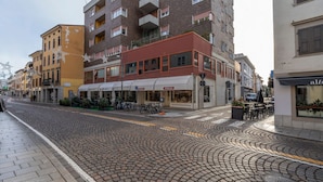 A cobblestone street with buildings, including a multi-story structure with balconies and a ground-level shop. - GuestHost - Cozy & Bright Apartment - w/ Balcony (udine)