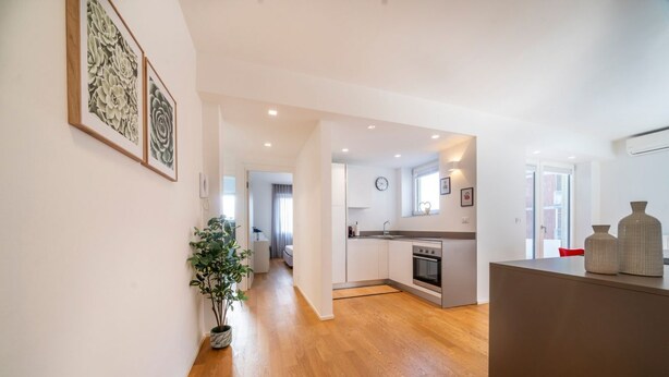 A modern kitchen with wooden flooring, a built-in oven, and a dining area with a red chair. - GuestHost - Cozy & Bright Apartment - w/ Balcony (udine)