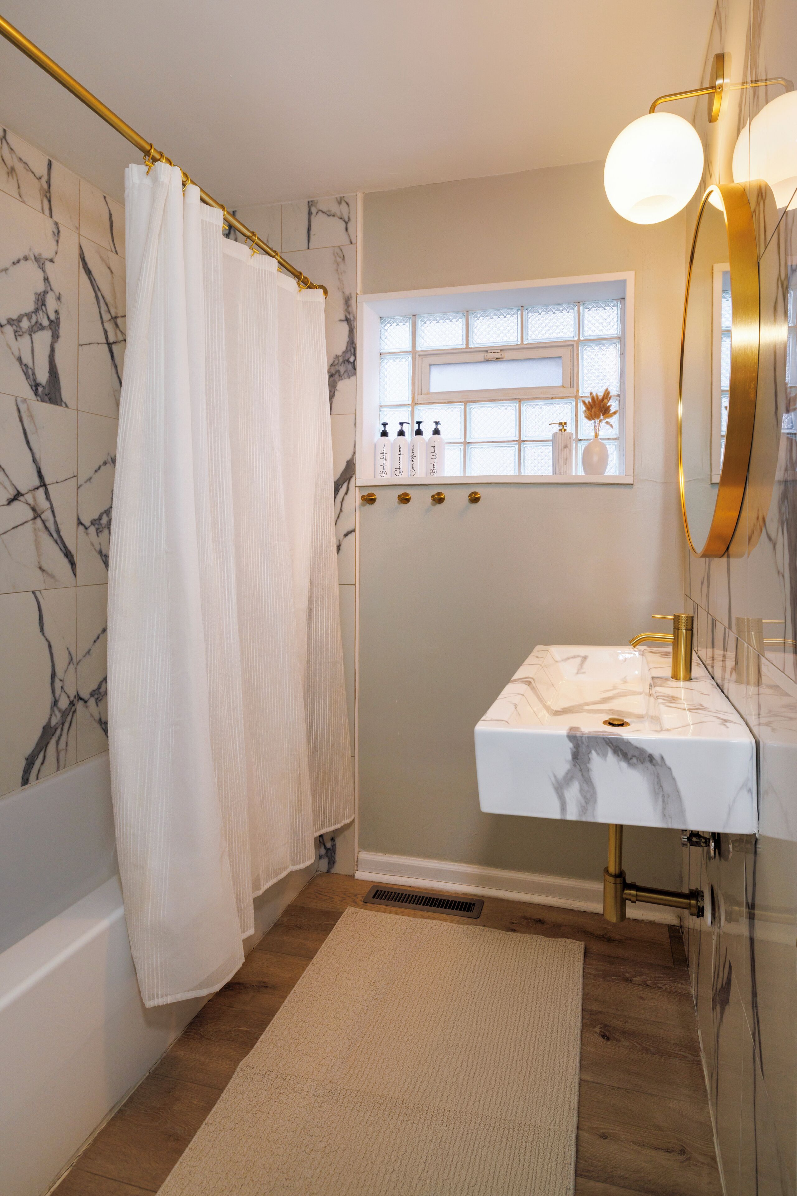 A bathroom with a shower curtain, a sink with a marble countertop, and a window with bottles on the wall.