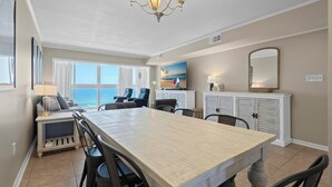 A dining area with a large table, chairs, a chandelier, a view of the ocean, and a seating area with a sofa and chairs. - GULF-FRONT VIEW, POOL, HEART OF GULF SHORES! (Gulf Shores)