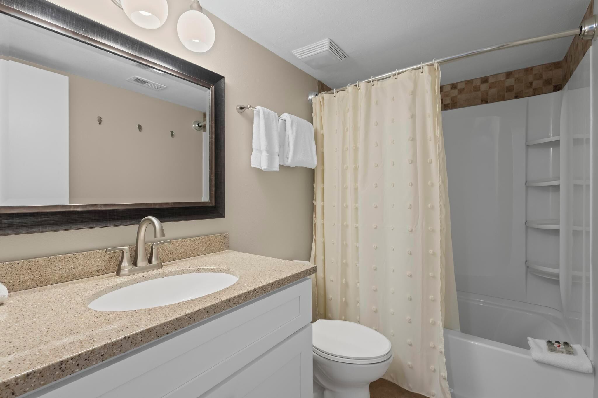 A bathroom with a sink, mirror, toilet, and shower area.
