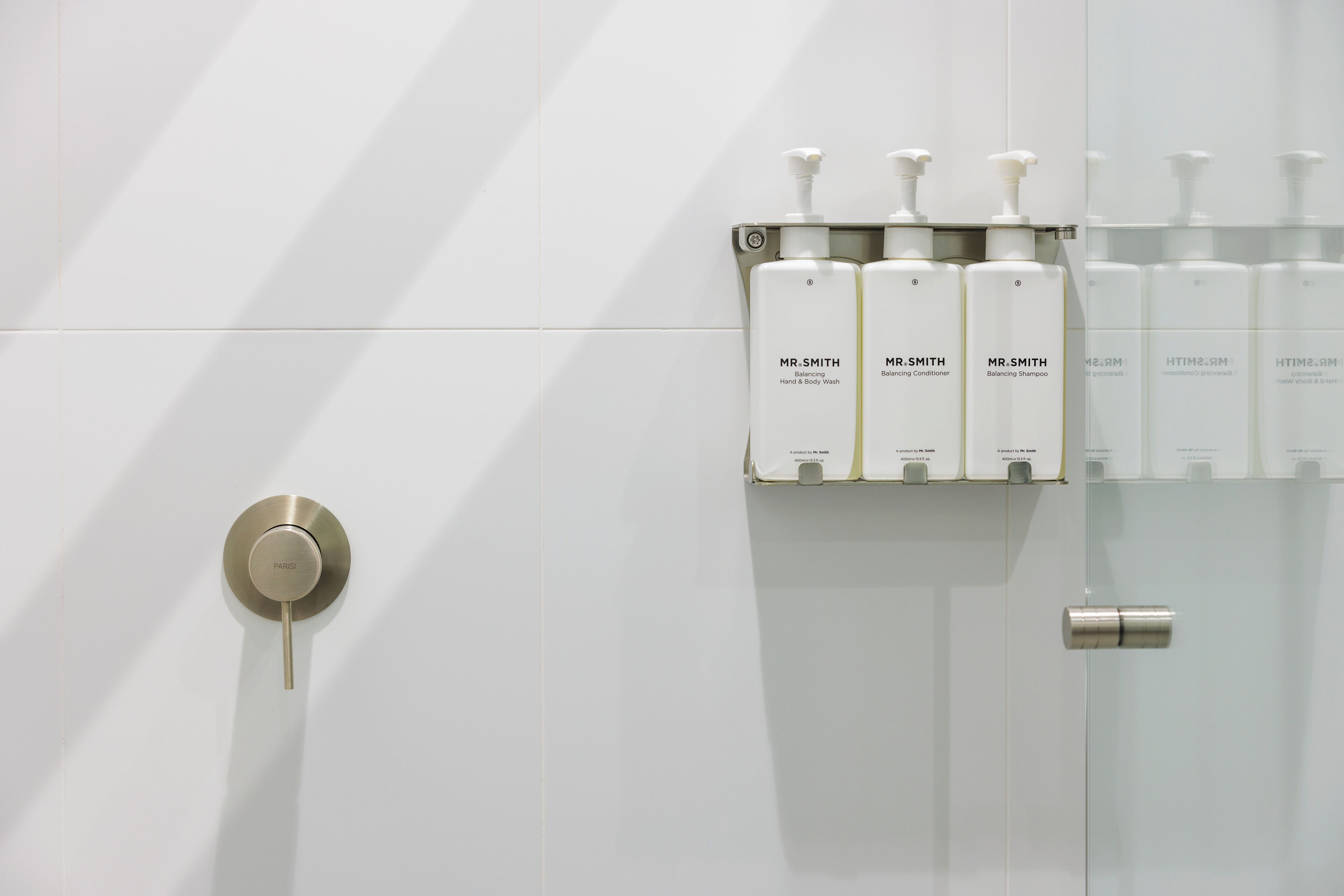 A bathroom with a modern design, featuring a toilet, a sink with a soap dispenser, and a mirror.