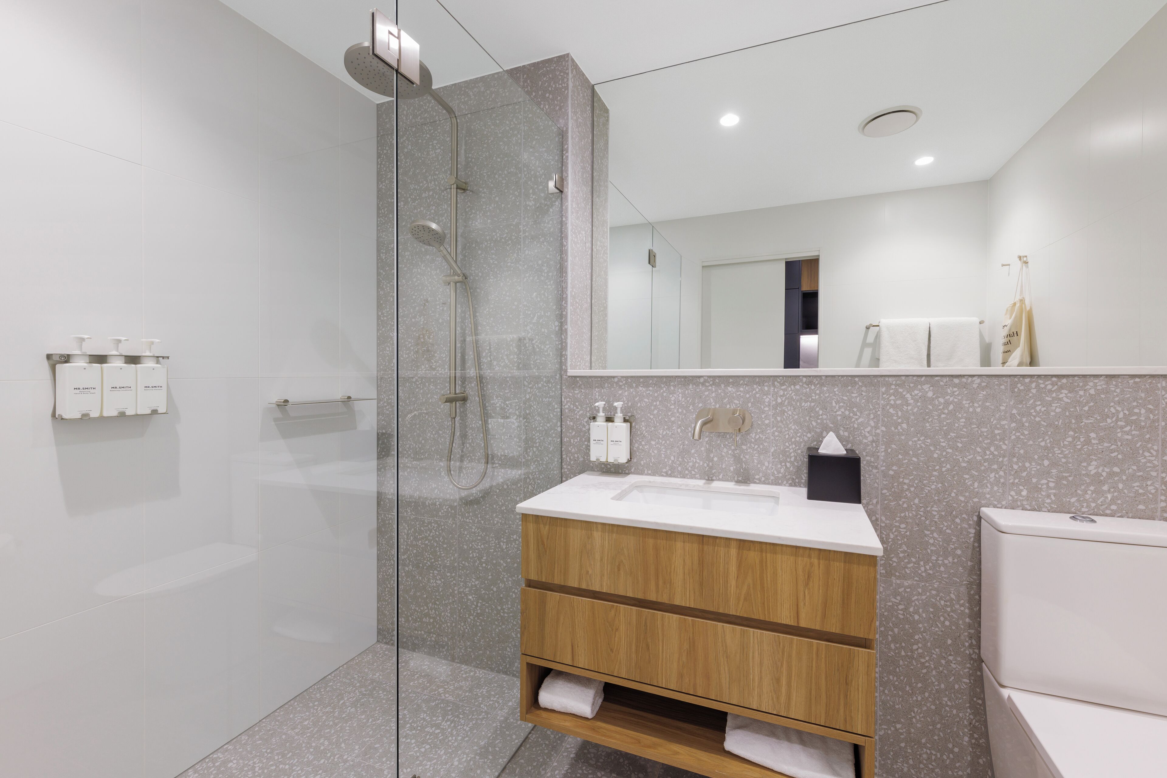 Un baño moderno con ducha de vidrio, tocador de madera con lavamanos y un inodoro.