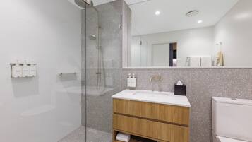 Un baño moderno con ducha de vidrio, tocador de madera con lavamanos y un inodoro.