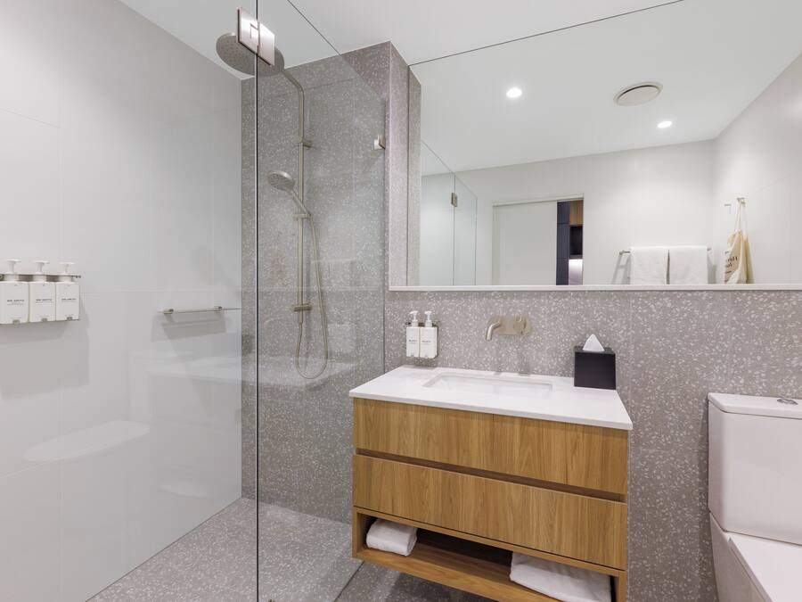 Un baño moderno con ducha de vidrio, tocador de madera con lavamanos y un inodoro.