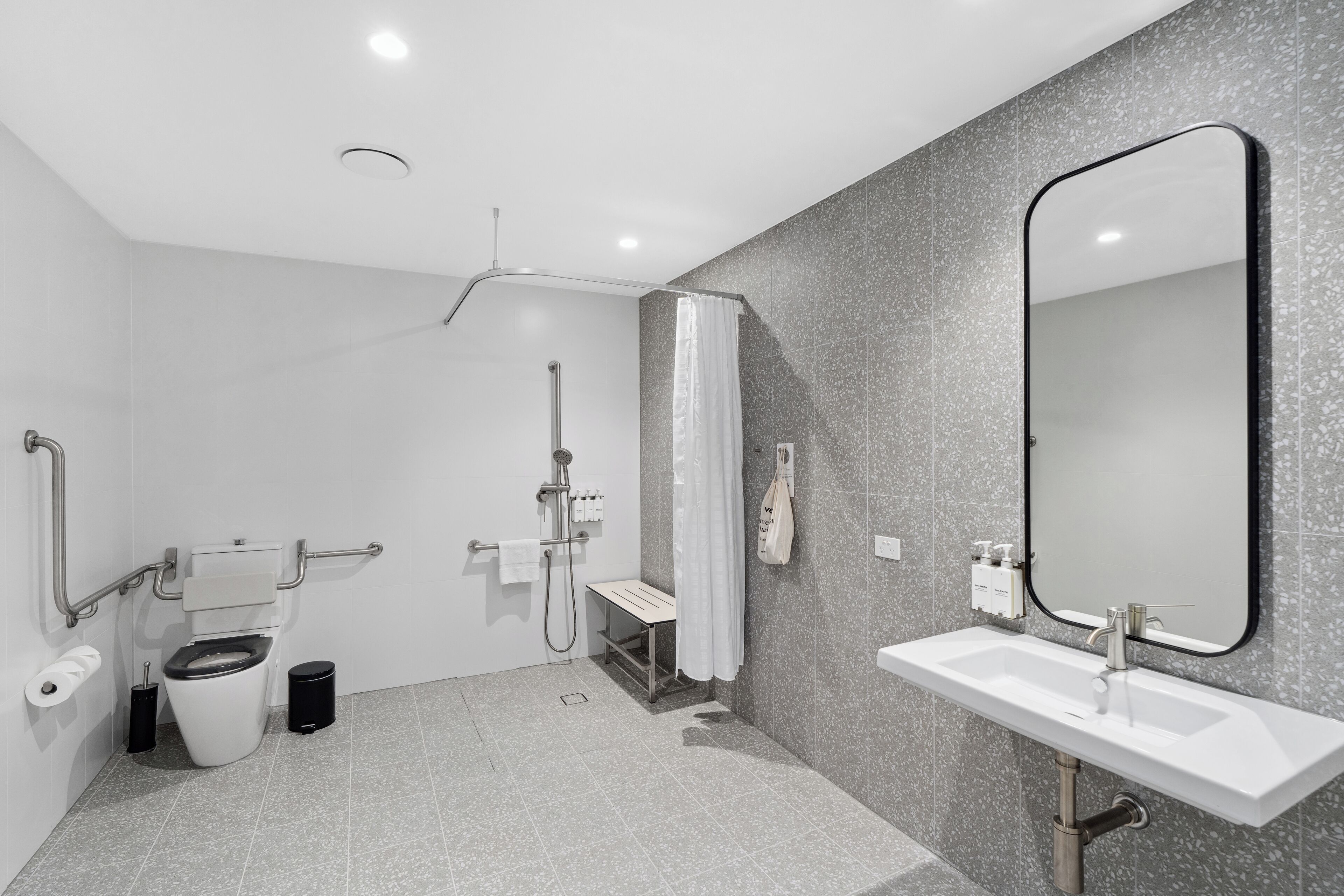 A modern bathroom with a toilet, sink, shower, and a large mirror.