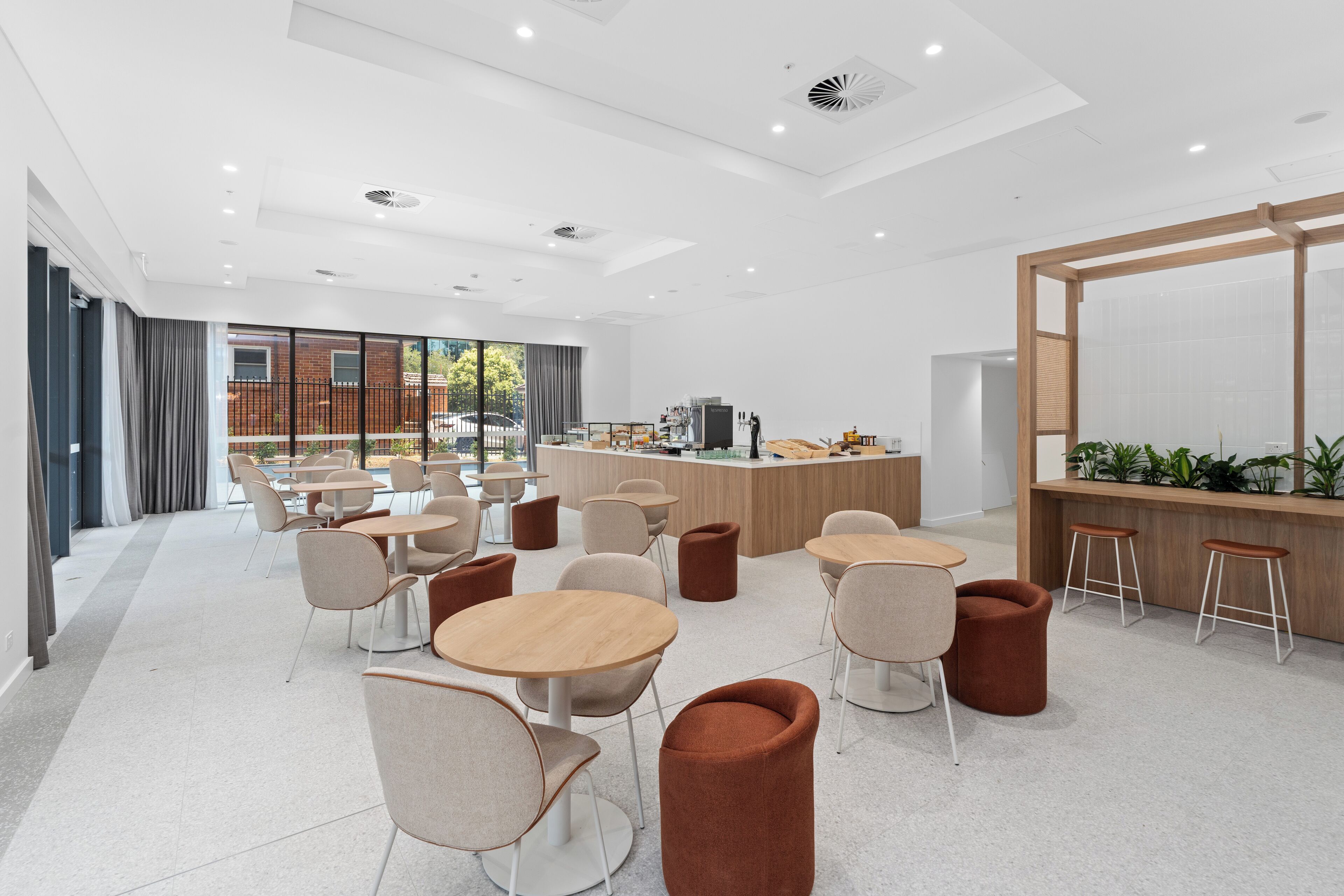 Un espace intérieur moderne avec des tables et des chaises rondes, un comptoir avec des tabourets et une vue sur un bâtiment en briques à travers de grandes fenêtres.
