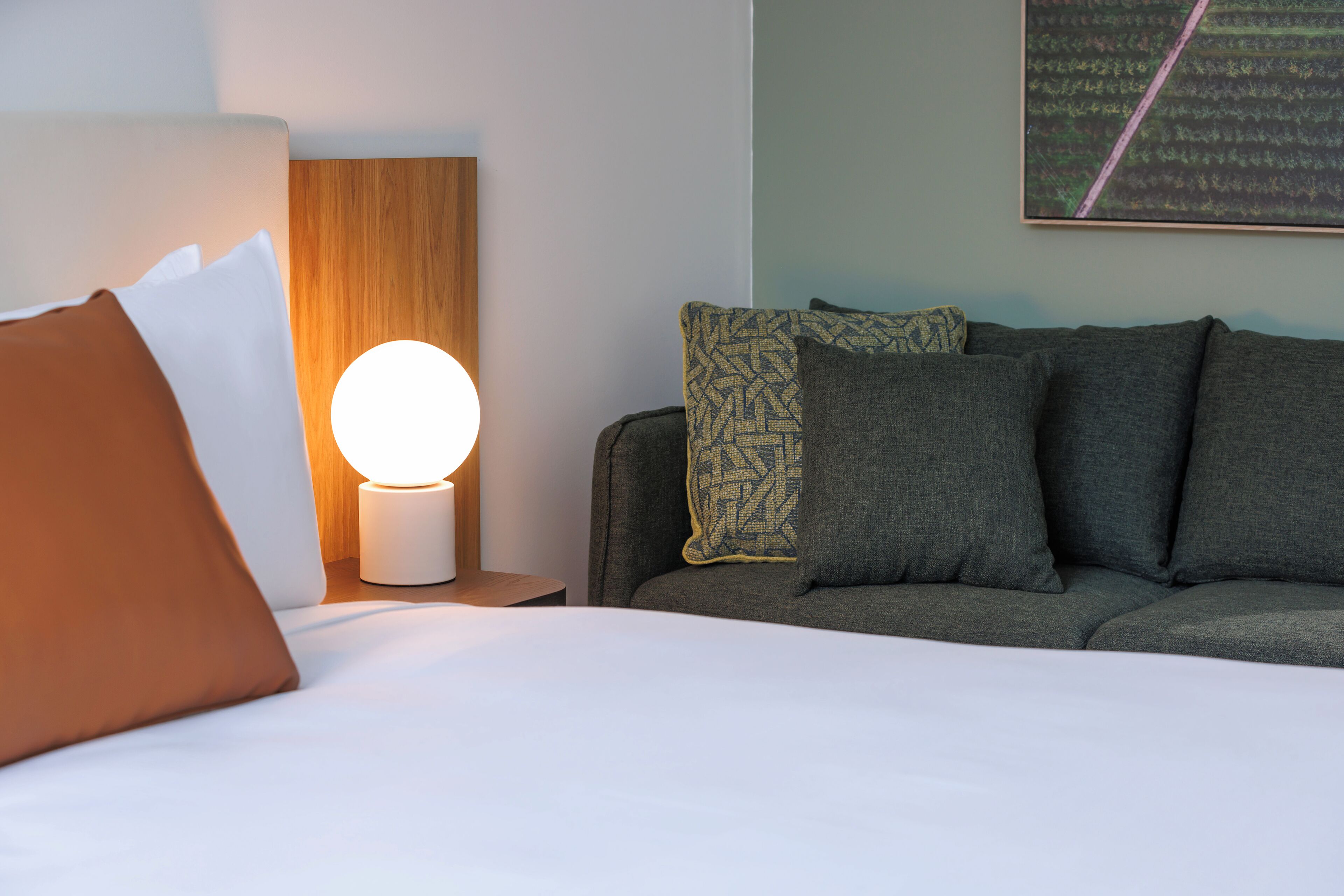 Un lit bien fait, avec du linge de lit blanc, et une lampe de table ronde posée à côté.