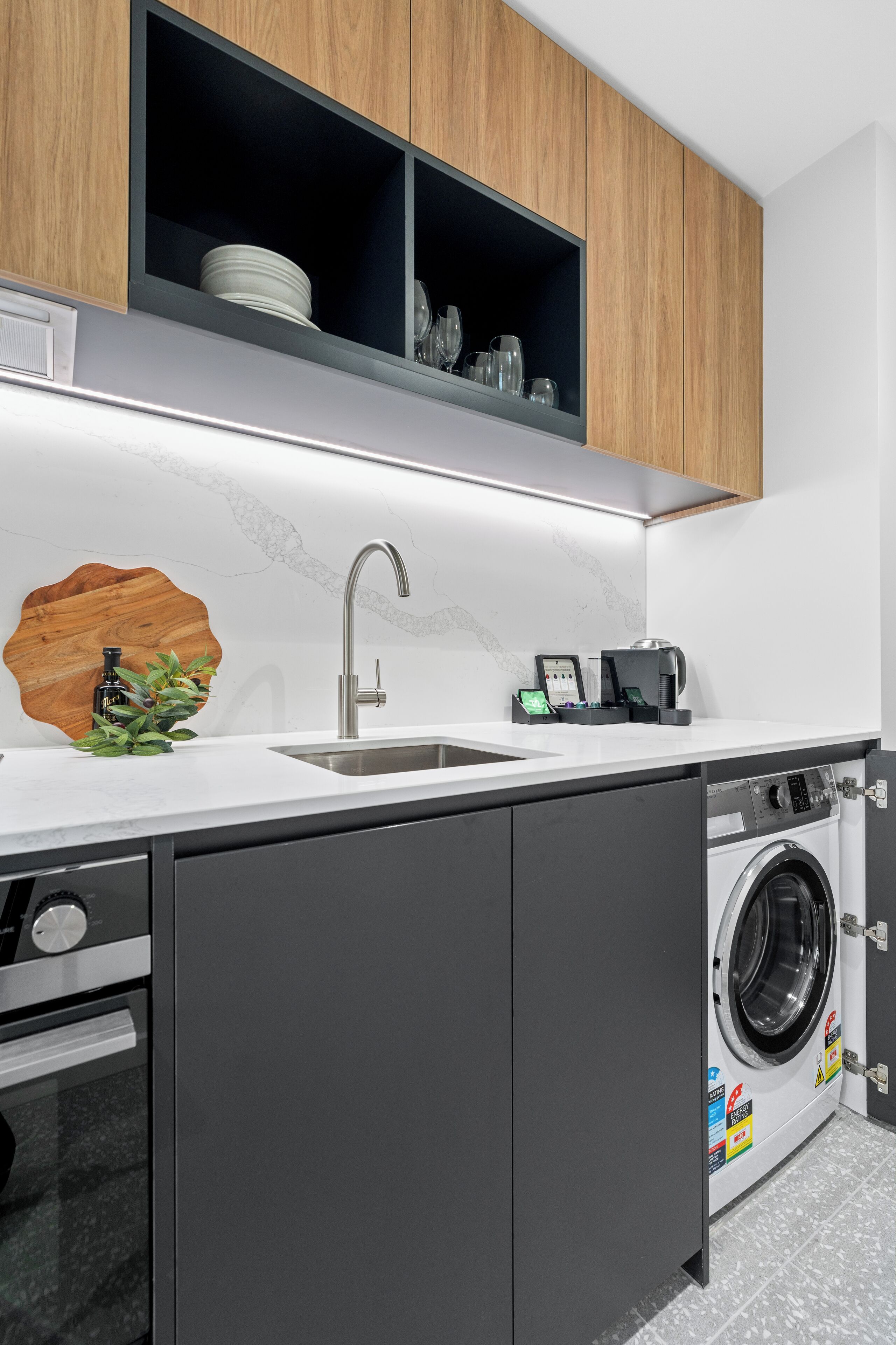 A compact kitchen with a built-in washing machine, a sink, and wooden cabinets above.