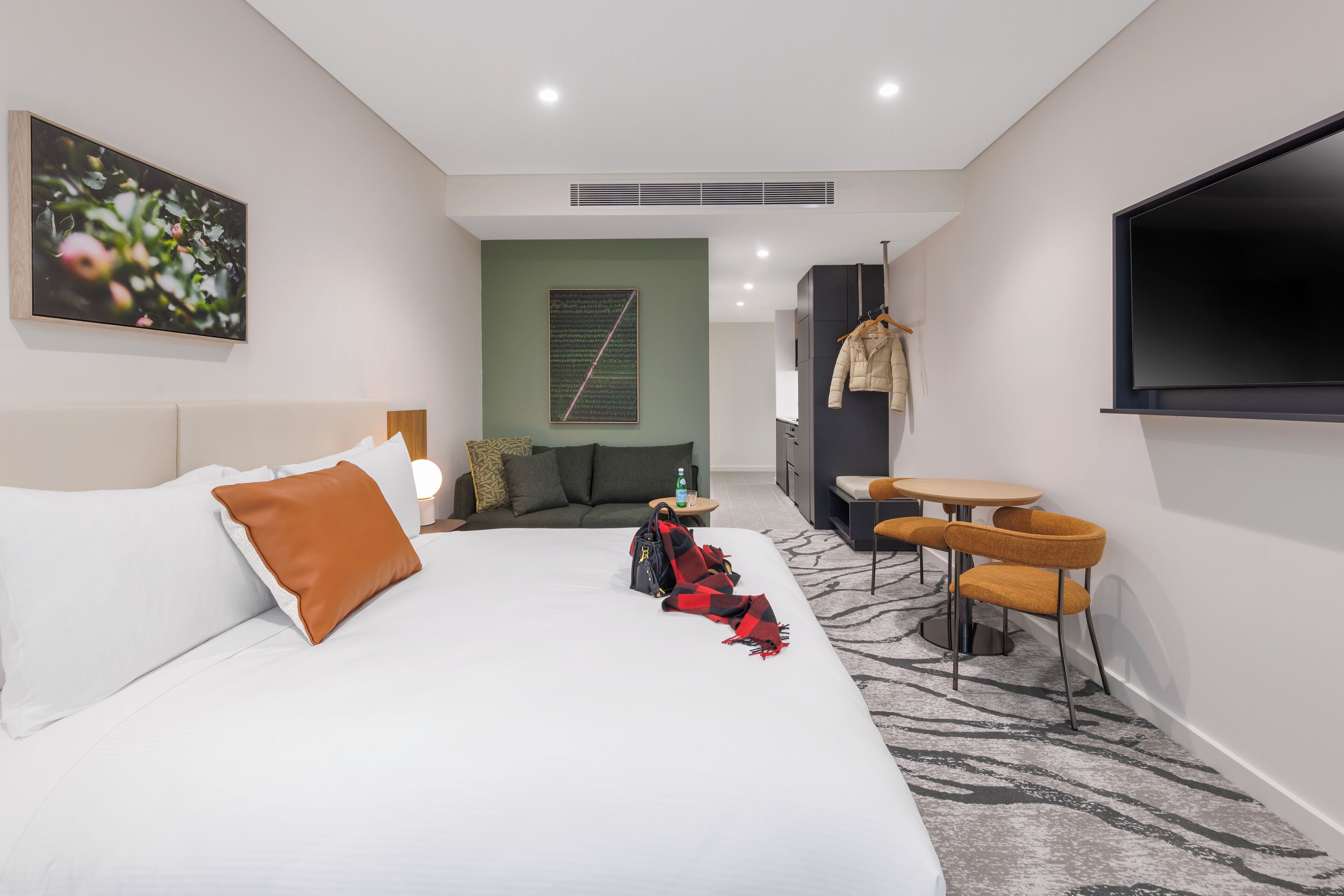 A hotel room with a bed, a sofa, a TV, a table with chairs, and a coat rack.