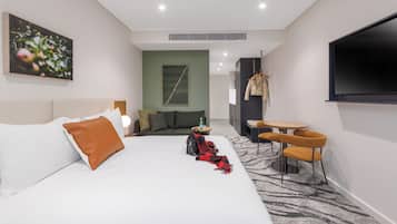Une chambre d’hôtel comprenant un lit, un canapé, une télévision, une table avec des chaises et un porte-manteau.