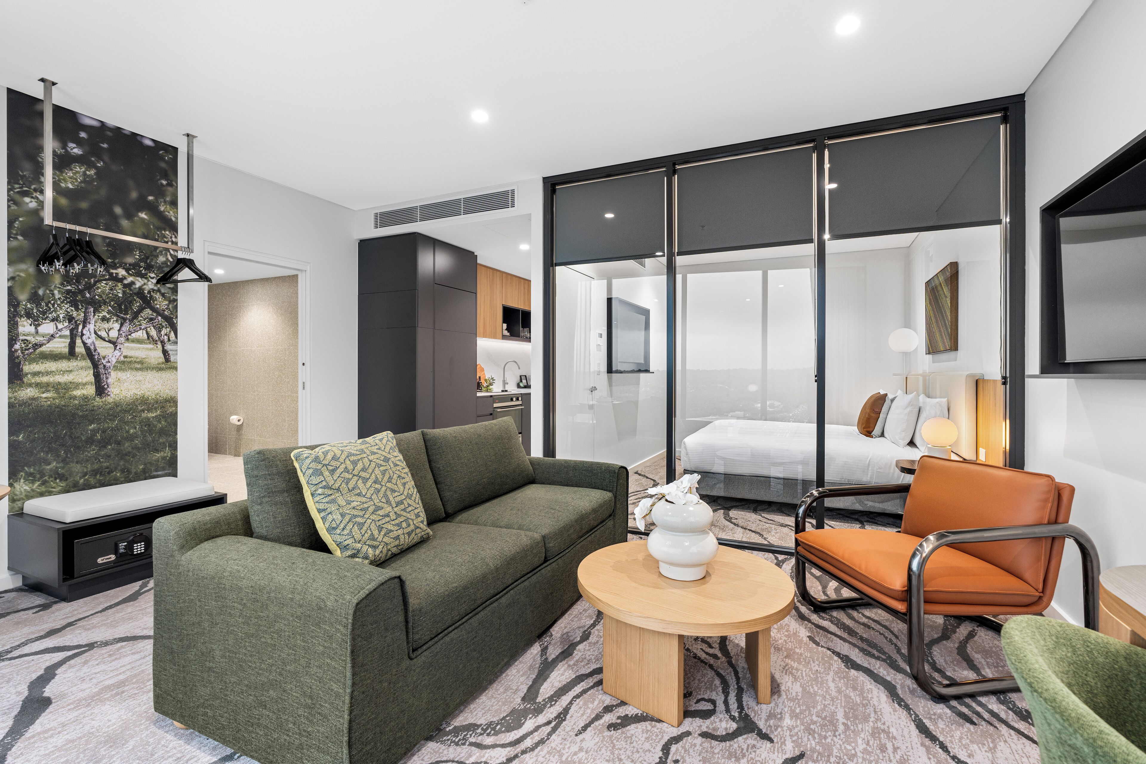 A modern living room with a sofa, a chair, a coffee table, and a bed in the background.