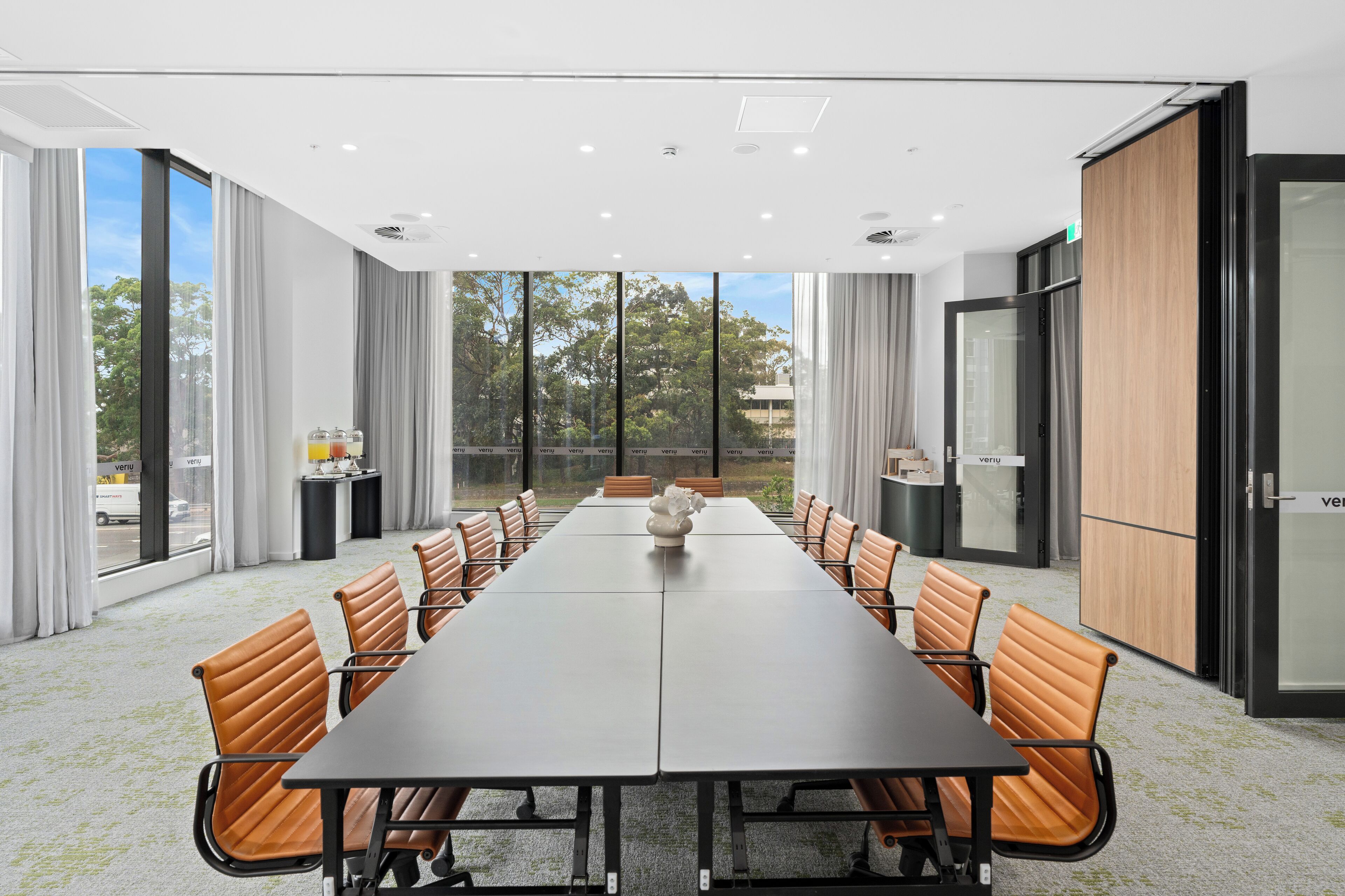 A conference room with a long table, leather chairs, and large windows offering a view of trees and buildings.