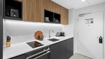 A modern kitchen with a built-in oven, a sink, and a microwave. There are wooden cabinets above the counter and a door with a lock on the right.