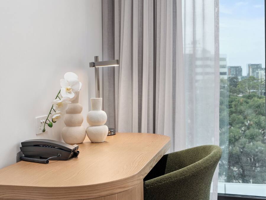 Ein modernes Hotelzimmer mit einem Holztisch, einem grünen Sessel, einem Telefon und dekorativen Vasen.