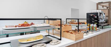 Un área de buffet con diferentes opciones de comida, una máquina de café y una vitrina de vidrio.