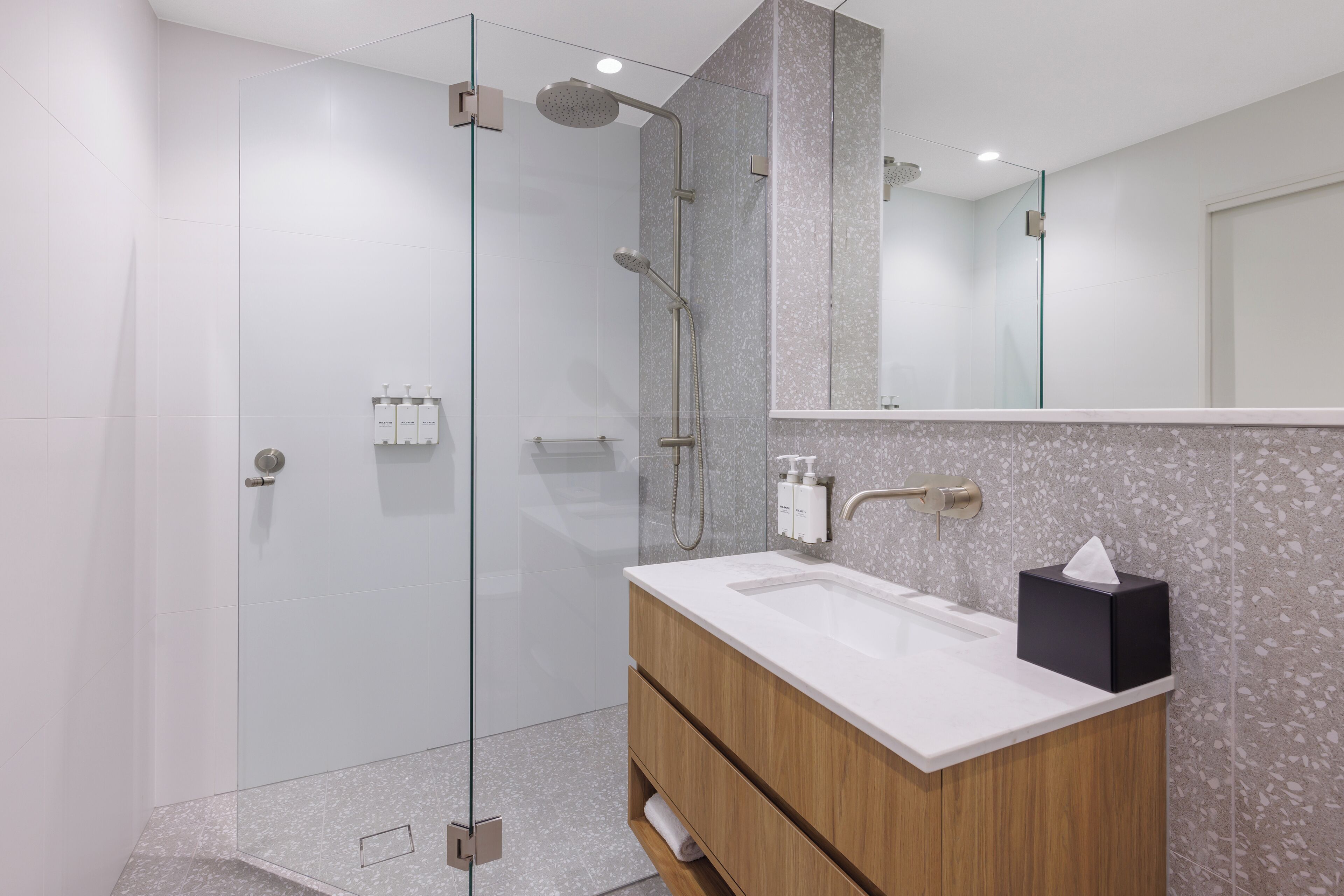 A modern bathroom with a glass-enclosed shower, a wooden vanity with a white sink, and a large mirror above the vanity.