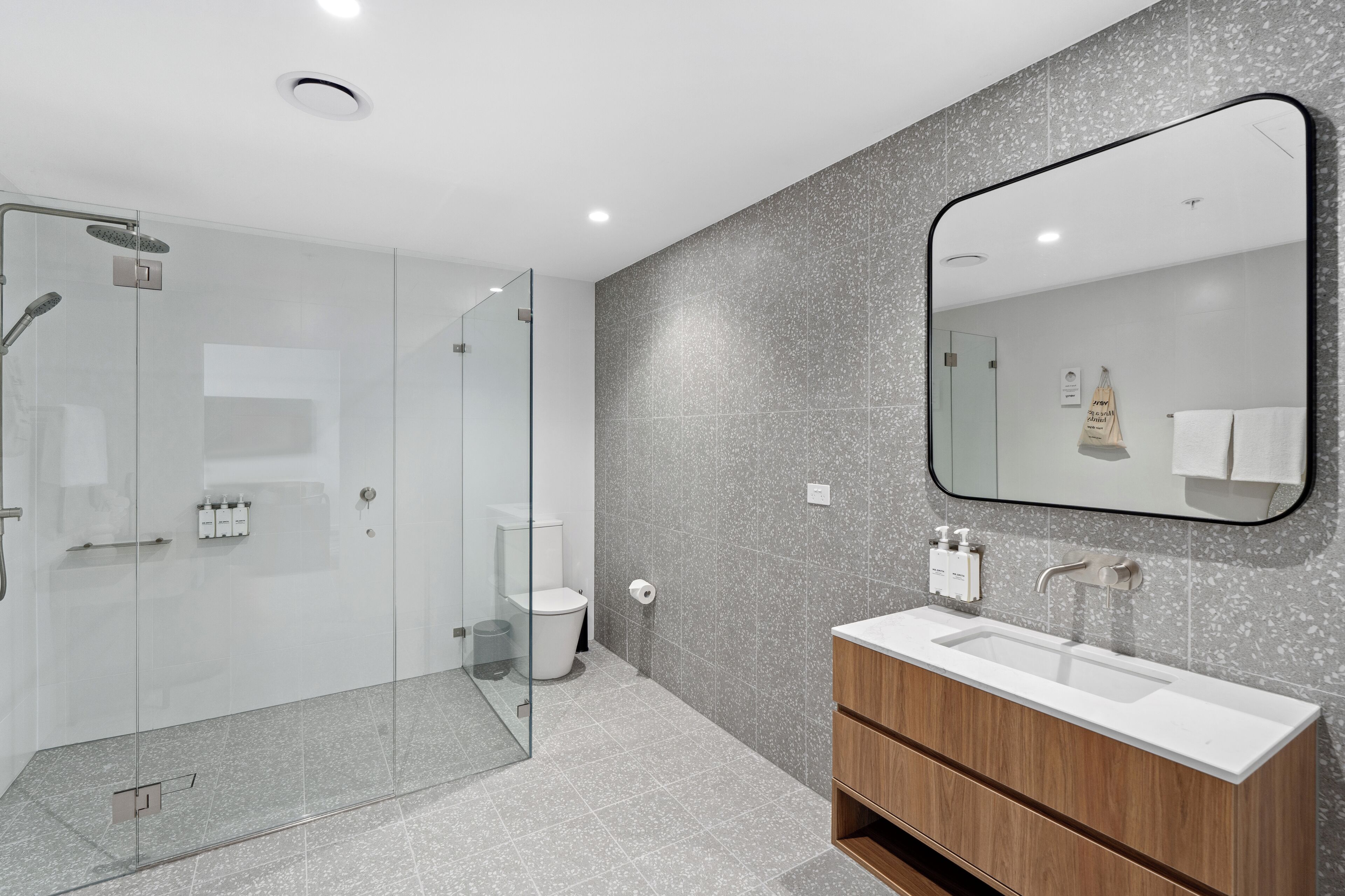 Un baño moderno con cabina de ducha de vidrio, un lavamanos blanco y un mueble de tocador de madera.