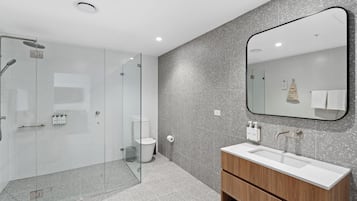Un baño moderno con cabina de ducha de vidrio, un lavamanos blanco y un mueble de tocador de madera.
