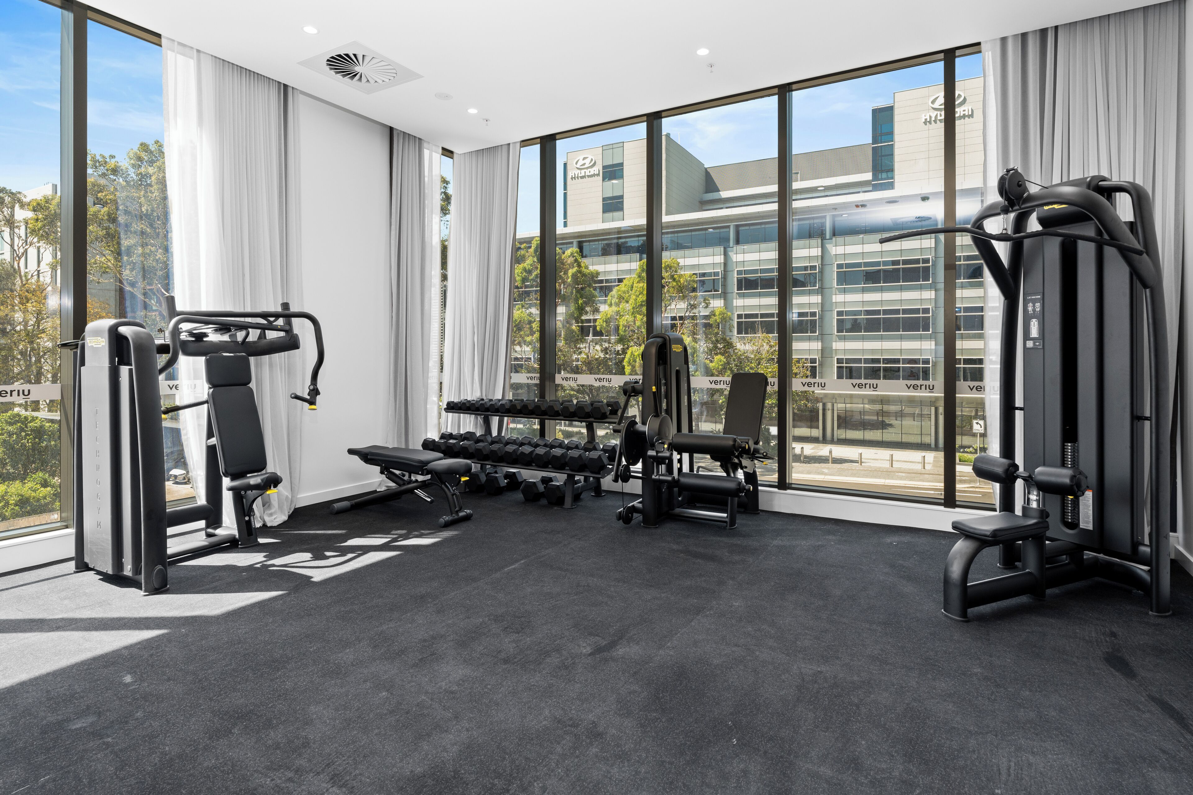 A gym with exercise equipment, large windows, and a view of a building.