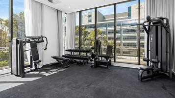 A gym with exercise equipment, large windows, and a view of a building.