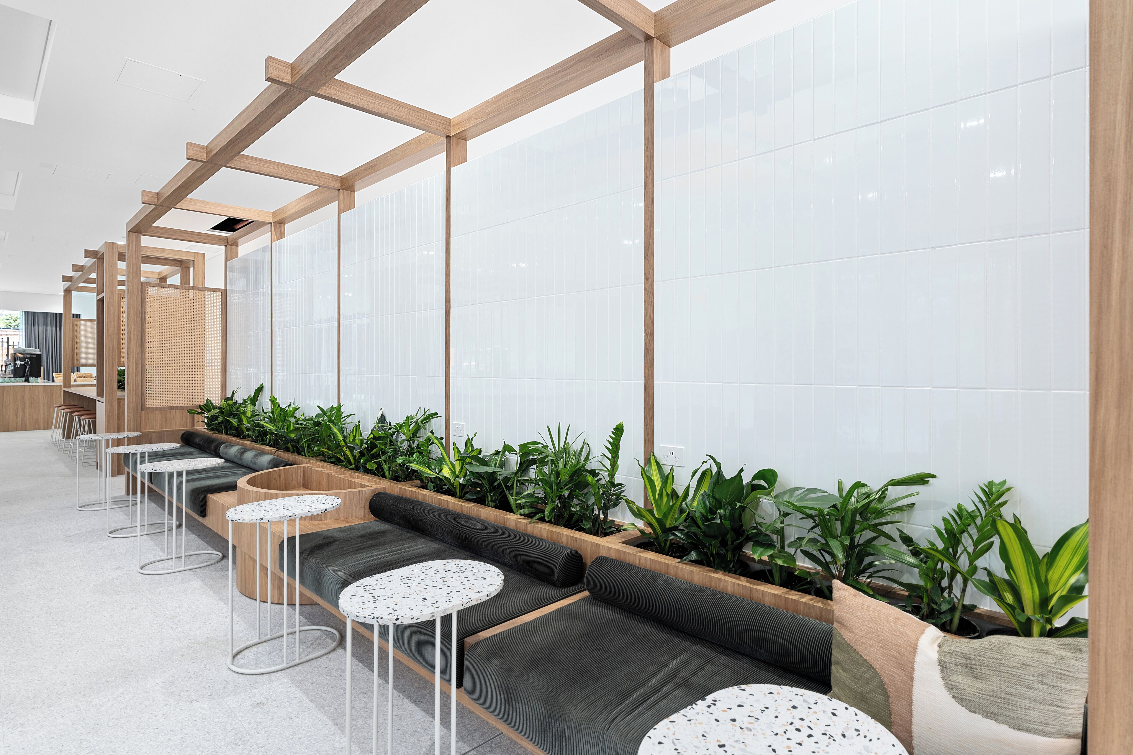 A modern waiting area with long benches, small round tables, and potted plants.