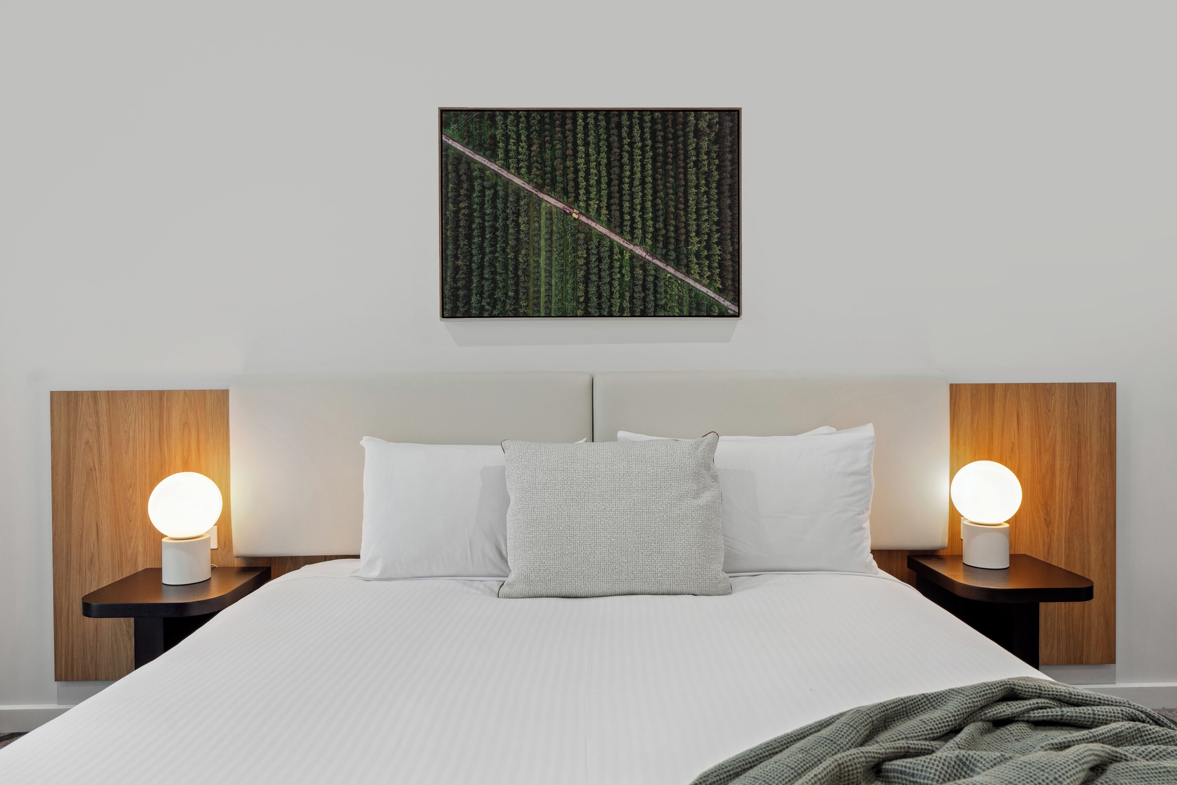 A neatly made bed with white linens and a gray pillow, flanked by two bedside tables with round, illuminated lamps.