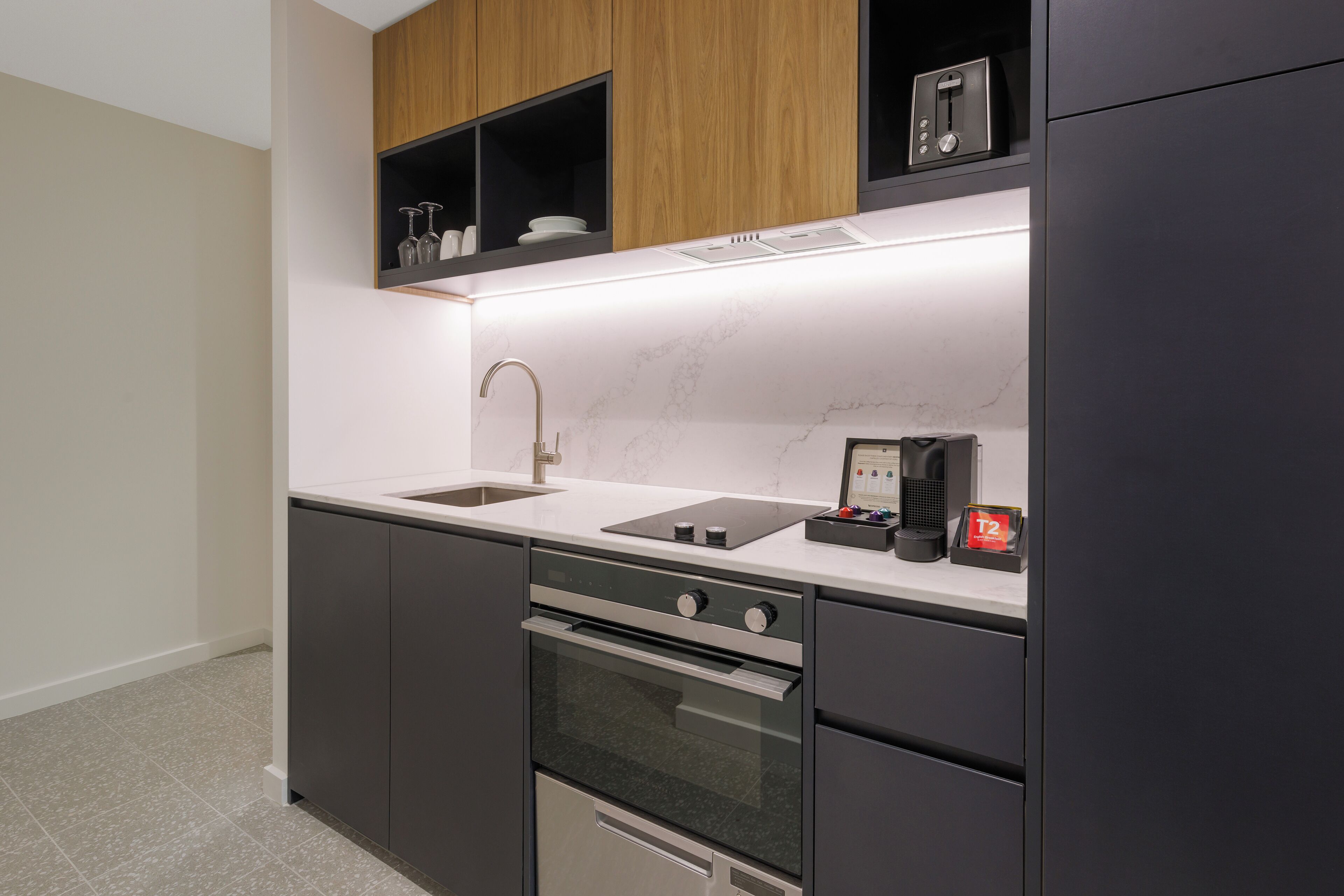 Una cocina moderna con horno de acero inoxidable, un lavamanos integrado y armarios de madera arriba.