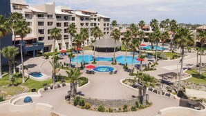 Ein Resort mit mehreren Schwimmbecken, Palmen und einem großen Gebäude mit Balkonen.