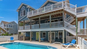 A two-story building with a pool, outdoor seating, and a balcony. - Laughing Duck: Pool, Walk Beach & Town, Dog-Friendly (Duck)