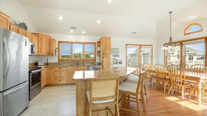 A spacious kitchen with wooden cabinets, a stainless steel refrigerator, and a large island with seating. - Laughing Duck: Pool, Walk Beach & Town, Dog-Friendly (Duck)