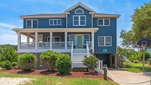 A two-story house with a porch, a basketball hoop, and a small garden area. - Laughing Duck: Pool, Walk Beach & Town, Dog-Friendly (Duck)