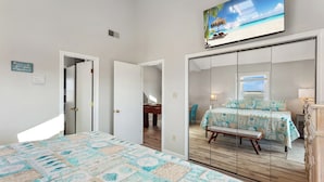 Un dormitorio con una cama grande, un escritorio, una silla y una ventana con vista a la playa.