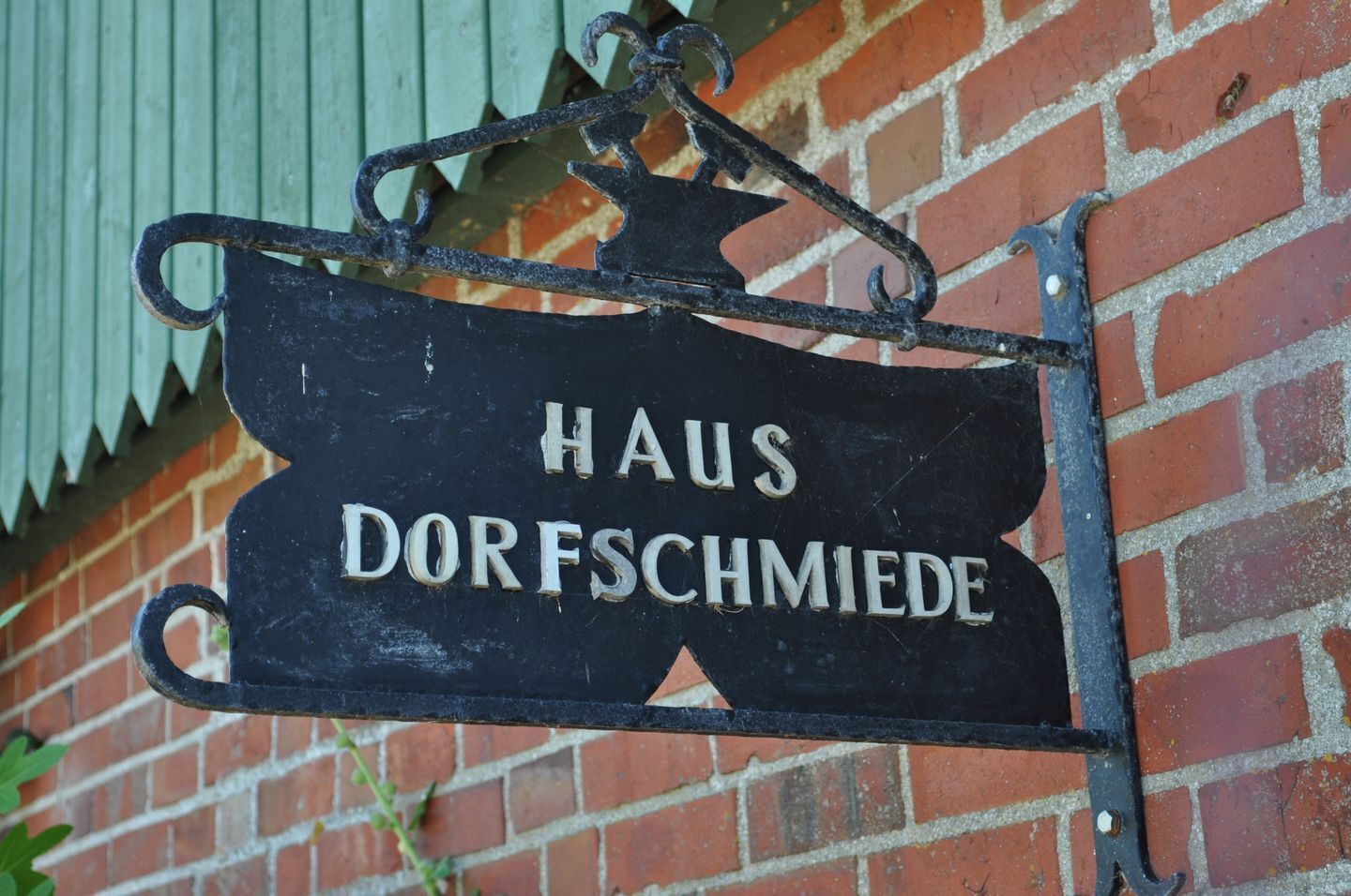 A black metal sign with the words 'HAUS DORFSCHMIDE' mounted on a brick wall.