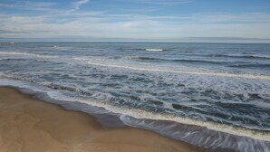 A beach with waves gently lapping onto the shore under a clear sky. - 2971 - Seabbatical - Duck Oceanfront Condo | Direct Beach Access (Duck)