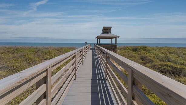 A wooden boardwalk leading to a gazebo with a slanted roof, surrounded by low vegetation and a clear sky. - 2971 - Seabbatical - Duck Oceanfront Condo | Direct Beach Access (Duck)