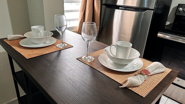 A dining table set with white dishes and glasses, a woven placemat, and a small cloth napkin.