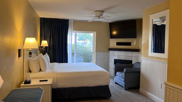 Una camera d'albergo con un letto, comodino, lampada, sedia, televisore e vista sull'esterno.