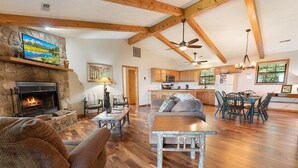 A spacious living room with a stone fireplace, wooden beams, a dining area, and a kitchen with wooden cabinets. - Little Little: Pet Friendly, Free Attraction Tickets, Hot Tub, Views & Hiking Trails (Sevierville)