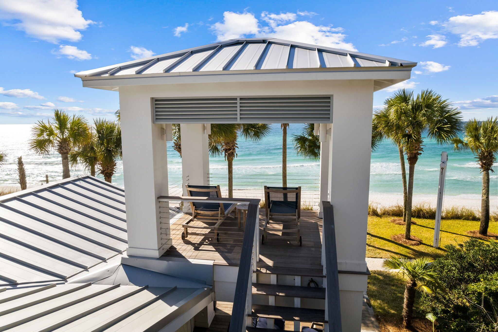 A gazebo with a view of the ocean, wooden furniture, and palm trees.