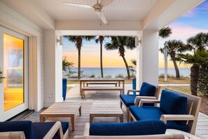 A covered outdoor seating area with wooden furniture and a view of the ocean at sunset. - Beach Front Seagrove Cottage in 30A (Santa Rosa Beach)
