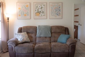 Un canapé marron avec des coussins à motifs, une lampe et trois affiches encadrées accrochées au mur.