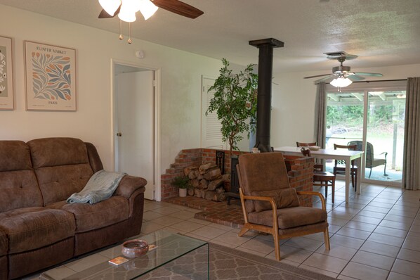 A living room with a sofa, armchair, glass coffee table, fireplace, and a dining area with a table and chairs.