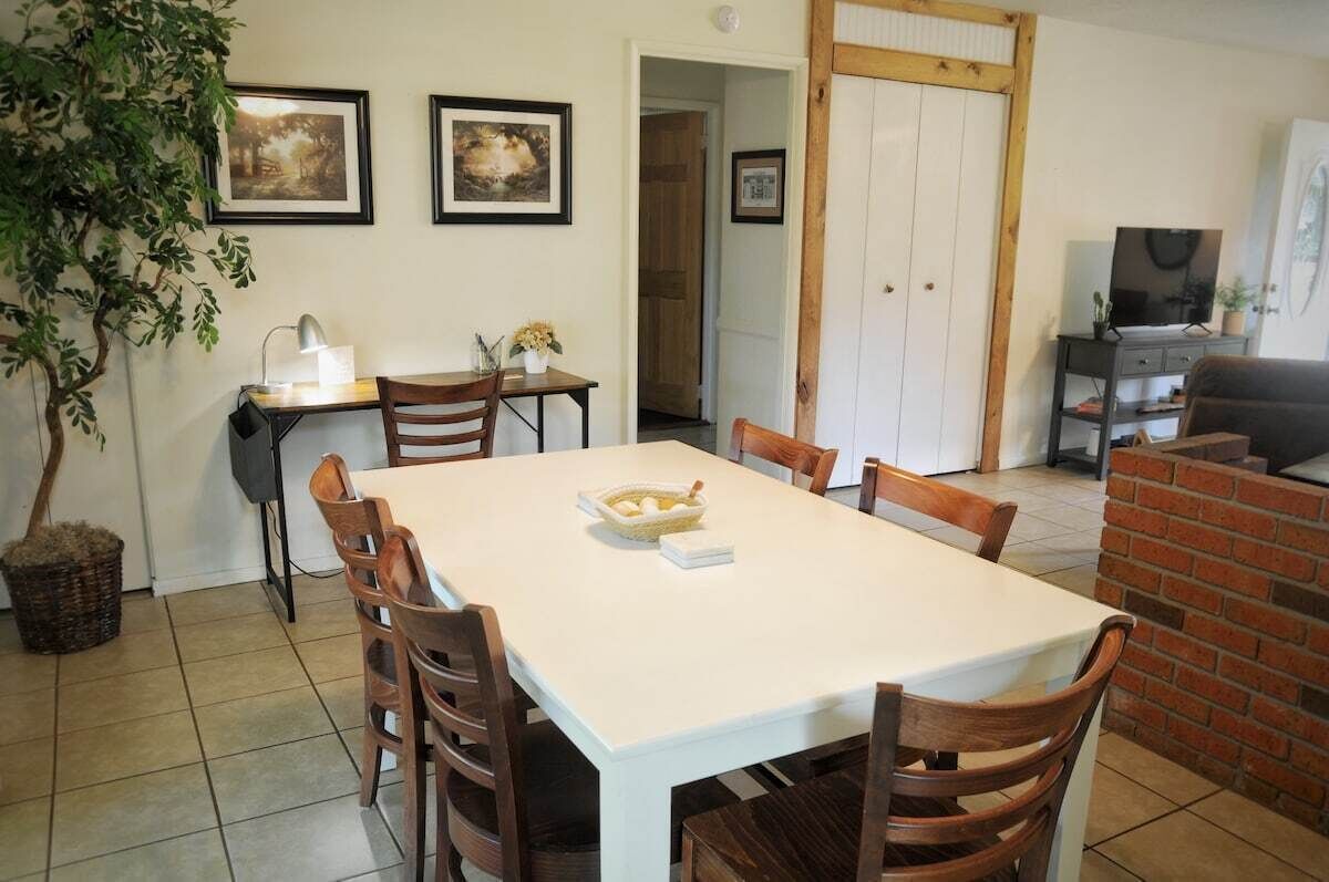A dining area with a white table and wooden chairs, a small side table with a lamp, and a basket on the floor.
