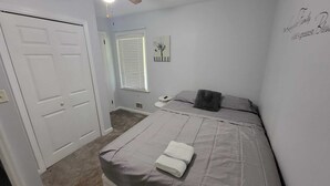 A bedroom with a bed, a bedside table, a window with blinds, a wall-mounted phone, and a door. - Cozy 3BR Lawrenceville Haven close to everything (Lawrenceville)