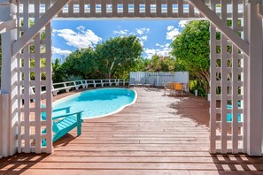 Eine Holzterrasse mit Pool, umgeben von einem weißen Zaun und Bäumen.