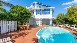 Una casa de dos pisos con piscina, sillas de deck y valla blanca.